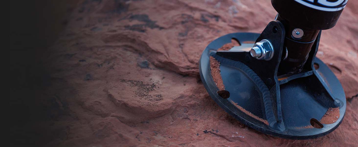 A close-up shot of AGMs patent GroundLoc Jack base pad, set against a textured reddish-brown rock surface.