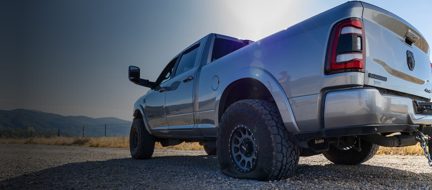 Ram 2500 pickup truck with a flat tire on a gravel road with mountains in the background
