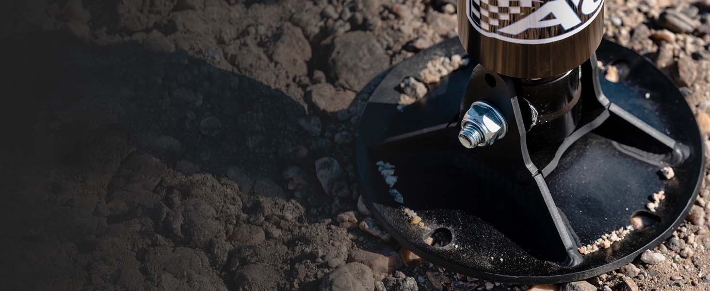 A close-up of AGMs patented GroundLoc jack base pad, set in rough dirt and gravel outdoors.