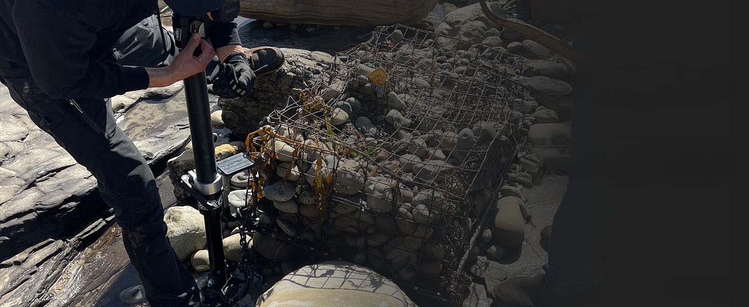 A person in dark clothing operates an AGM Electric Jack to remove stuck debris during a beach clean up event.  
