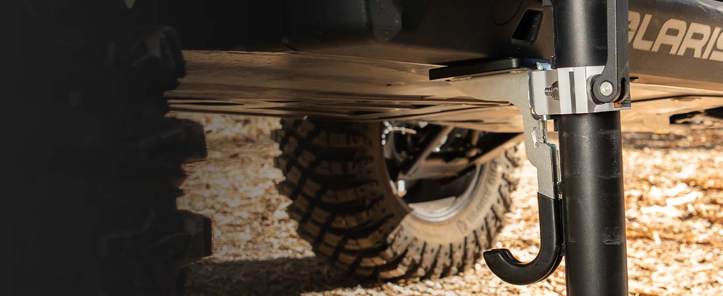 Close-up of an AGM Universal hook picking up under a vehicle frame, with a rugged tire and gravel ground visible.