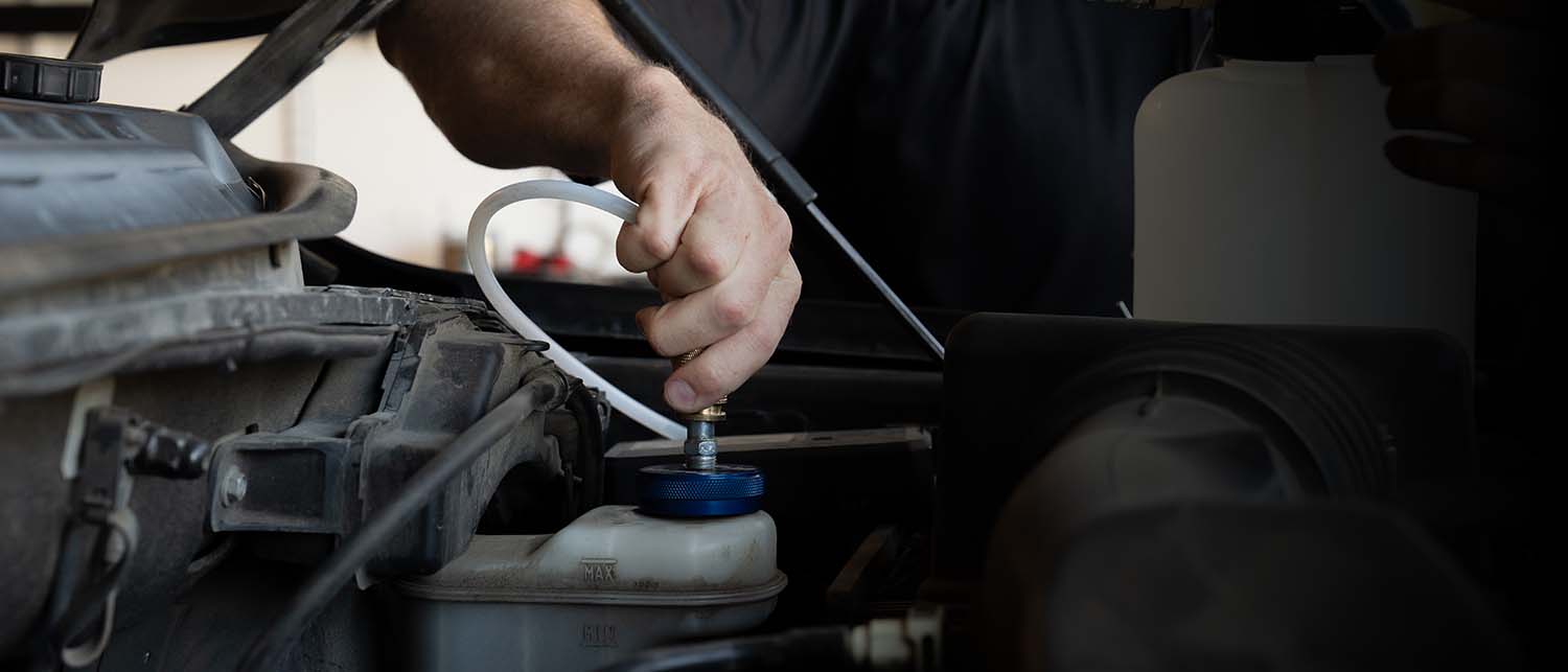 A close-up of a person's hand connecting an AGM Brake Pressure Bleeder hose to a blue AGM reservoir adapter cap.